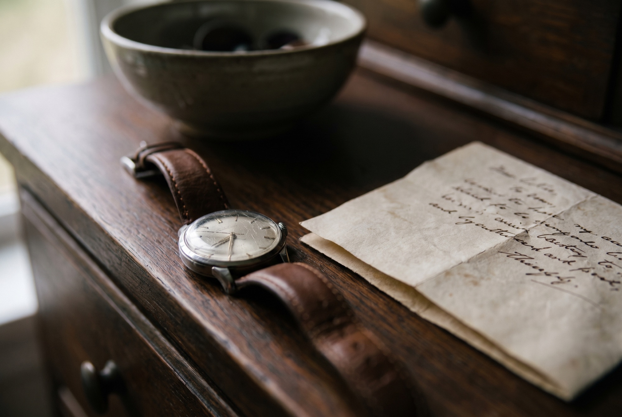 An old wristwatch and a folded handwritten letter on a wooden dresser