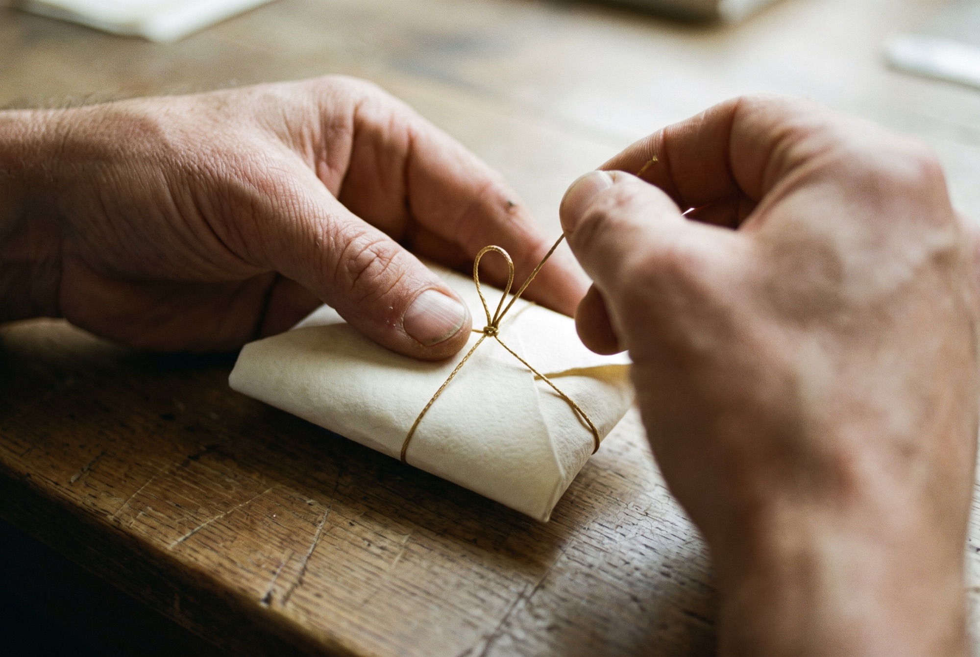 Hands tying a wrapped piece with antique gold thread